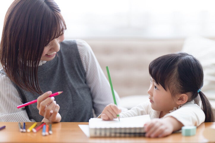 คุณแม่และลูกสาวขณะนั่งวาดภาพระบายสีด้วยกันบนโต๊ะ