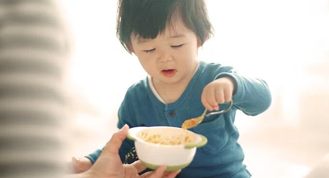 เด็กชายวัยหัดเดินกำลังฝึกทานอาหารด้วยตัวเอง ซึ่งเป็นเมนูเสริมธาตุเหล็กที่จำเป็นต่อพัฒนาการสมองและร่างกาย