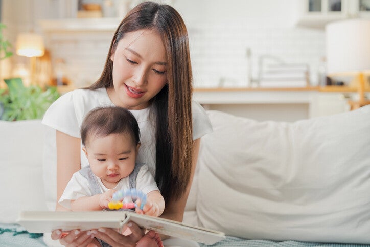 แม่ประคองลูกบนตักพร้อมอ่านหนังสือให้ลูกฟัง