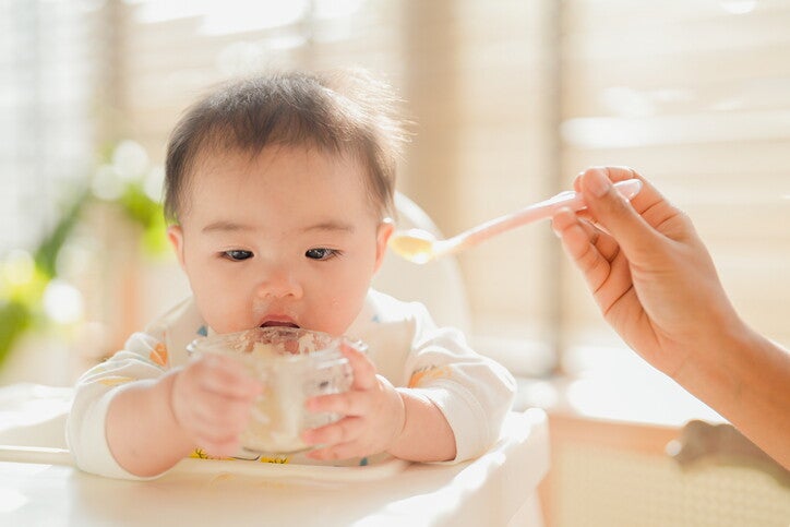 มือผู้ปกครองกำลังป้อนอาหารเด็กให้ทารกที่นั่งบนเก้าอี้สูง