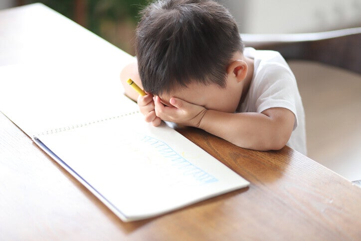 เด็กชายตัวน้อยก้มหน้าซบลงกับฝ่ามือด้วยความรู้สึกเหนื่อยล้าหรือหงุดหงิดขณะกำลังวาดภาพ