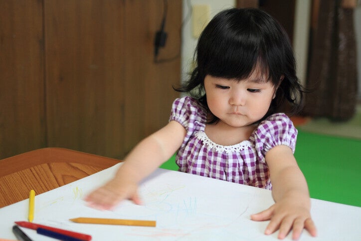 เด็กหญิงกำลังสนุกกับการขีดเขียนและระบายสีลงบนแผ่นกระดาษ