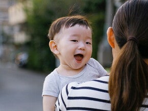 เด็กชายยิ้มกว้างอย่างร่าเริงขณะที่แม่กำลังอุ้มพาดบ่า