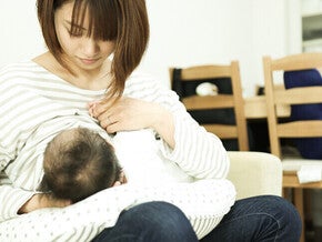 Photograph of a mother breastfeeding her baby on a couch in a bright living room