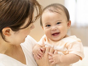 แม่อุ้มเด็กทารกที่กำลังยิ้มกว้างจนเห็นฟัน