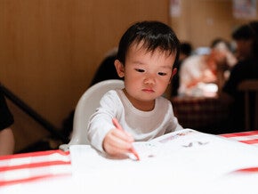 เด็กชายระบายสีด้วยสีเทียนสีแดงลงบนกระดาษ