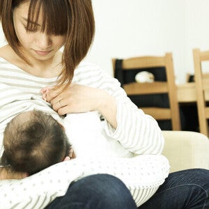 Photograph of a mother breastfeeding her baby on a couch in a bright living room