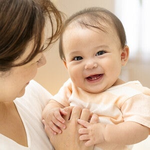 แม่อุ้มเด็กทารกที่กำลังยิ้มกว้างจนเห็นฟัน