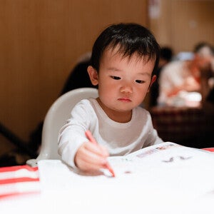 เด็กชายระบายสีด้วยสีเทียนสีแดงลงบนกระดาษ