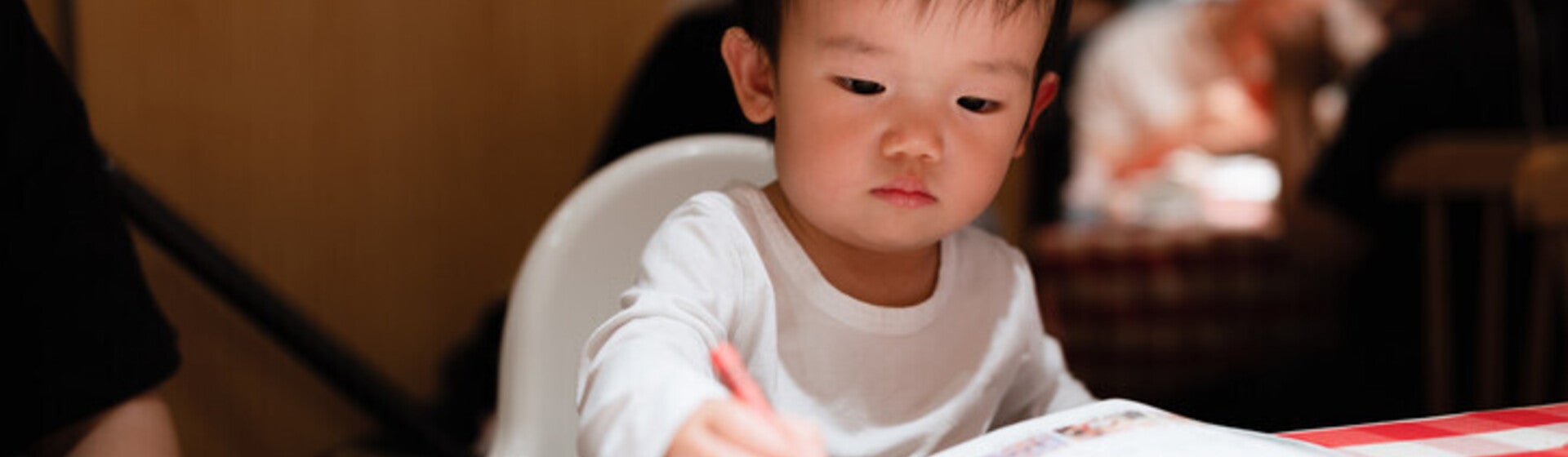 เด็กชายระบายสีด้วยสีเทียนสีแดงลงบนกระดาษ